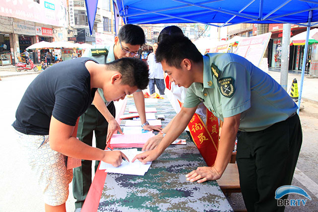 寧明縣徵兵辦工作人員正在為現場報名應徵的適齡青年指導填寫報名表